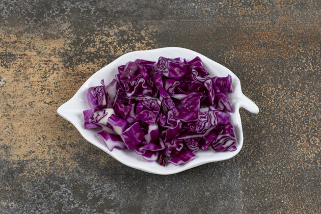 健康的切碎的卷心菜放在叶子形状的盘子里 放在大理石表面新鲜美味蔬菜