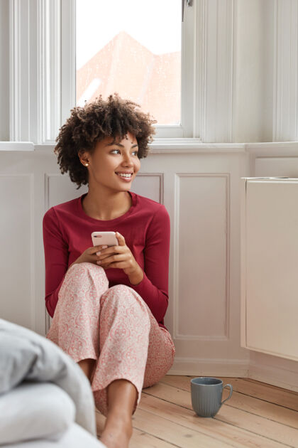 坐着一个穿着睡衣 面带微笑的黑皮肤女人 手里拿着现代手机 在网上共享文件成功使用短信