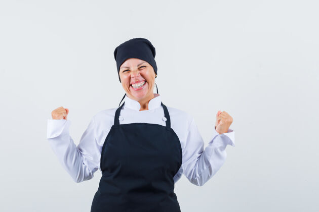 新鲜金发女人的肖像 展示赢家的姿势在黑色厨师制服 看起来很漂亮的前视图自然成人黑发