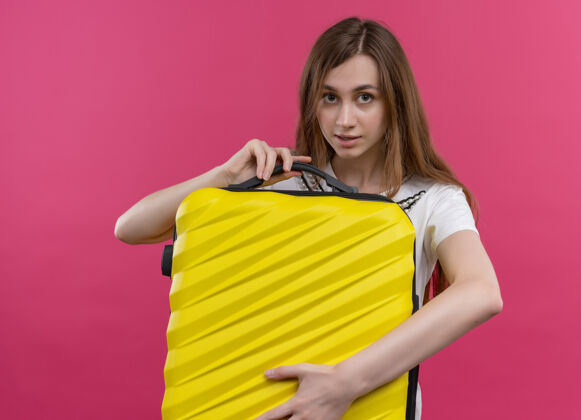 年轻人年轻的旅行女孩拿着手提箱 看着孤立的粉红色墙壁拿着女人女孩