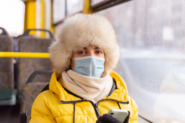 旅行一幅阳光明媚的肖像画 描绘了一个冬天 穿着暖和衣服 手里拿着手机 坐在城市公共汽车上的年轻女子车票公共温暖