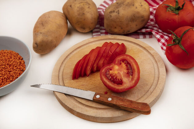 扁豆木制厨房板上的红色西红柿切片俯视图 刀子上放着橙色小扁豆 碗里的整个西红柿和土豆被隔离在白色墙壁上的格子布上视图板食品