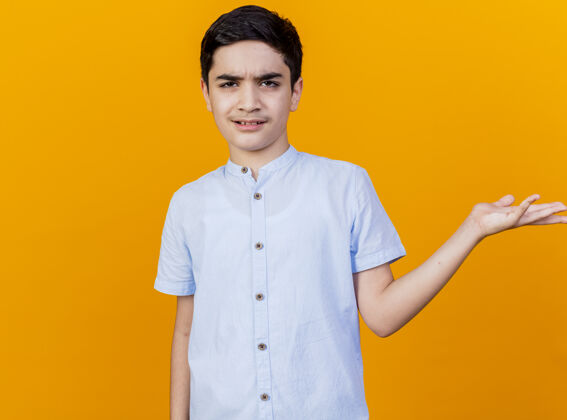 年轻皱着眉头的年轻白人男孩看着相机 在橙色的背景上显示出孤立的空手 还有复印空间空间显示橙色