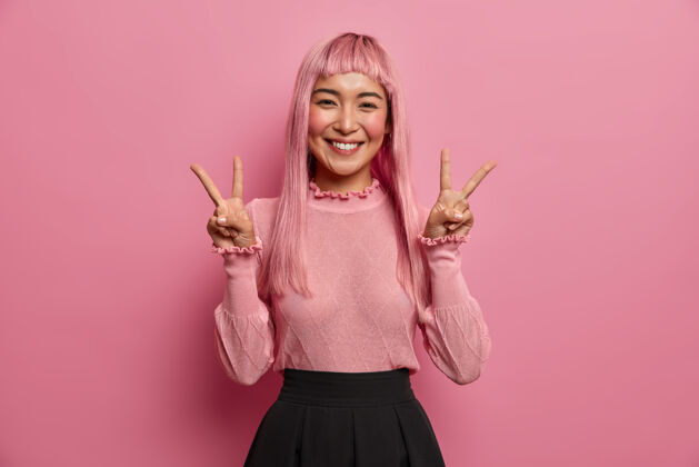 人快乐兴奋的亚洲年轻女子 长着粉红色的头发 摆出胜利的手势 伸出两个手指 积极地微笑美丽粉红色假发情绪