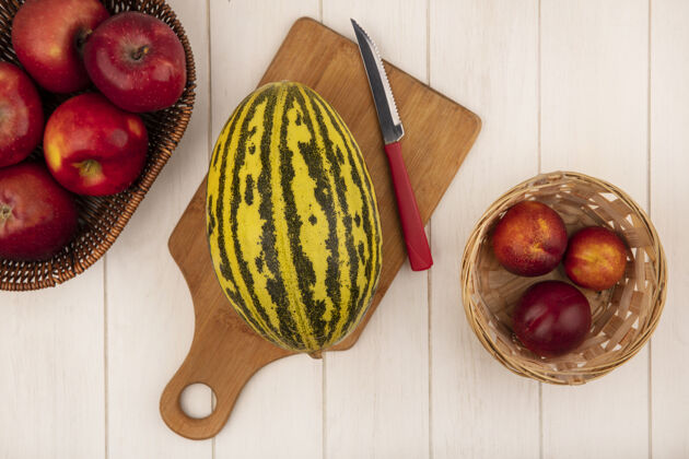 厨房新鲜的哈密瓜在一个木制的菜板上的俯视图 刀上放着苹果 桶上放着桃子 白色的木墙上刀苹果夏天
