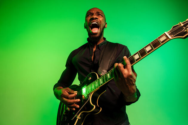 帅气年轻的非洲裔美国音乐家 在渐变的绿黄色背景下像摇滚明星一样弹吉他音乐会成人表演