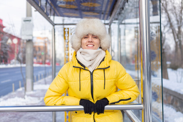城镇在寒冷的日子里 一个穿着冬衣的女人在公共汽车站等公共汽车电车围巾等待