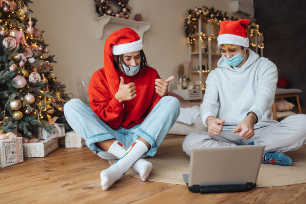 呼叫两个朋友在笔记本电脑附近的圣诞帽是通过视频通话互动礼物活动房子