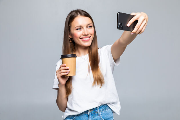 塑料办公室里用智能手机自拍 喝着塑料杯外卖咖啡的女人的画像魅力欢呼套装