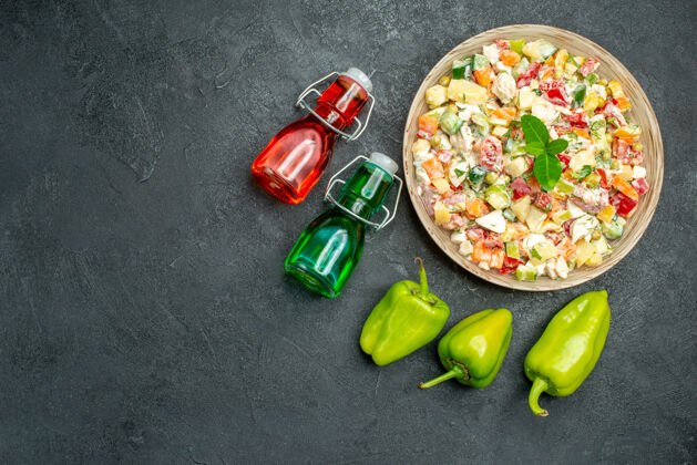 素食深绿色桌子上一碗蔬菜沙拉的顶视图 里面有甜椒 油和醋瓶饮食铃铛蔬菜