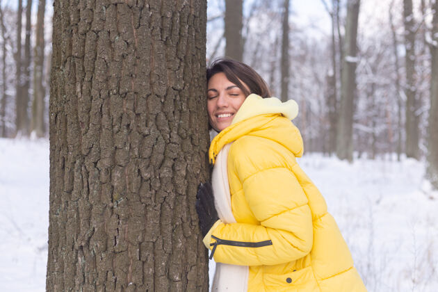 环境美丽的年轻女子在冬天的森林里表现出对大自然的柔情 表现出对树的爱人休闲年轻