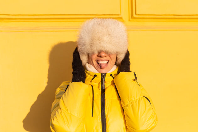 欢呼在阳光明媚的日子里 一个戴着温暖的俄罗斯西伯利亚帽子的快乐女人的肖像画 她在冬天穿着雪白的zabas 对着黄色的墙壁微笑着手套华尔街女孩
