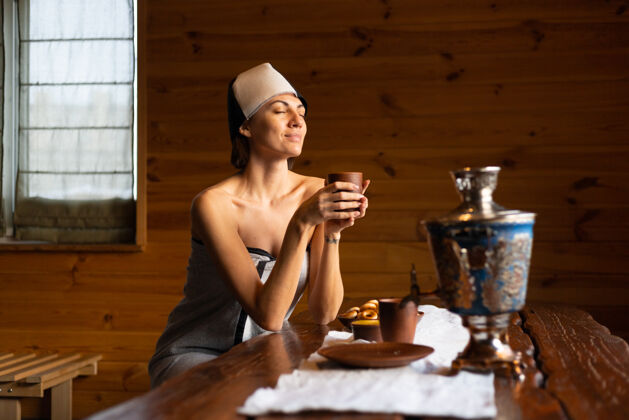 护理一个戴着帽子的年轻女子坐在一张桌子旁 喝着花草茶 享受着健康的一天桑拿治疗茶