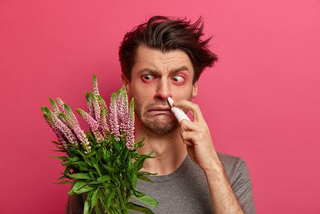 封闭过敏的男人有花粉热 他的免疫系统对外来物质有反应 眼睛红肿 用滴鼻剂进行有效治疗 站在室内季节性过敏和流汗的概念季节人人