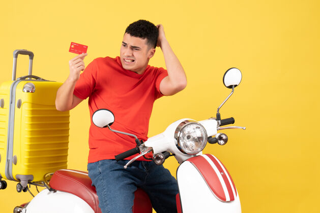 活跃前视图困惑的年轻人穿着红色t恤在轻便摩托车持卡T恤轻便摩托车微笑