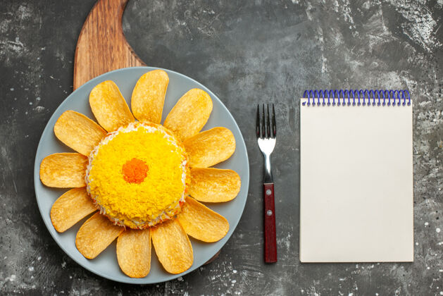柑橘沙拉的顶视图在中间 盘子架在下面 叉子和记事本放在深灰色的桌子上架子深色记事本