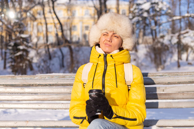 肖像一个冬天的女人 穿着暖和的衣服 在一个阳光明媚的日子里 坐在长凳上 冻得浑身发冷 冬天很不开心 一个人拿着咖啡担心冻结成人