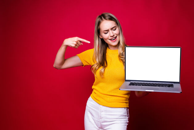 使用面带微笑的年轻女子的画像被指在隔离在红墙上的笔记本电脑屏幕上笔记本电脑笔记本电脑手