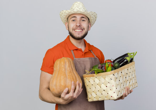 男面带微笑的男园丁戴着园艺帽捧着南瓜和菜篮看着持有帽子复制