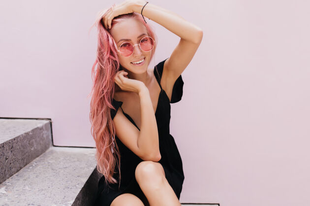 欧洲快乐的年轻女士穿着优雅的衣服坐在楼梯上笑着配饰粉色头发人