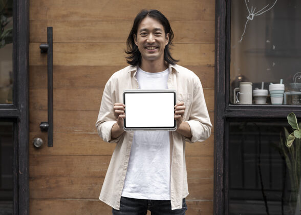 展示一个日本男人在他家门口展示一个数字平板电脑屏幕亚麻衬衫中年数字平板电脑