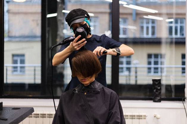 发廊一个专业的女理发师给客户理发这个女孩戴着面具坐在美容院里脸肖像理发师