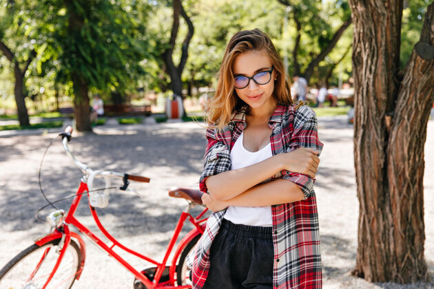 活动夏日里 一个穿着格子衬衫的高加索女孩在公园里摆出一副有趣的姿势骑自行车后 一个幽默的金发女人在发抖道路健身骑车人