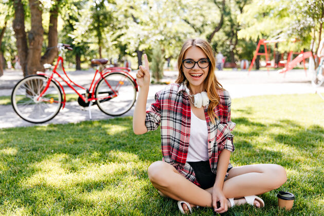 阳光幽默的年轻女子坐在草地上 带着真诚的微笑快乐的白人女孩在公园里的户外照片活跃草自行车