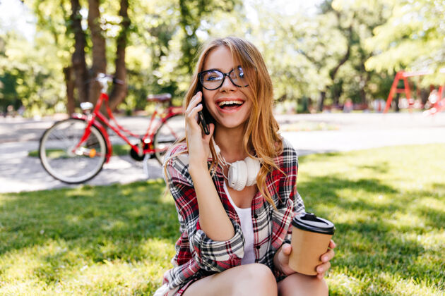 自行车在公园里欢笑的女孩在打电话在夏日里戴着眼镜的欧洲女人在给朋友打电话女性活跃阳光