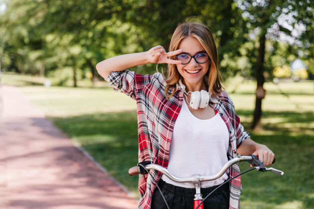 年轻可爱的女孩戴着大耳机在公园里转来转去一张可爱的女士坐在自行车上的照片树自行车田野