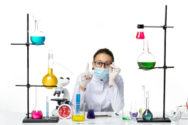 医学前视图：穿着医疗服的女化学家戴着口罩坐在白色背景上病毒化学实验室covidsplash飞溅视图医生
