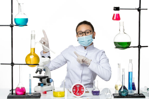 科学前视图穿着医疗服的女化学家带着面罩坐在浅白背景上的解决方案化学病毒covid-飞溅病毒医生医学
