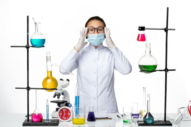 化学正面图：身穿医疗服的女化学家 戴着口罩 站在房间里 白色背景上的溶液 病毒化学实验室 covid-splash面罩实验室视图