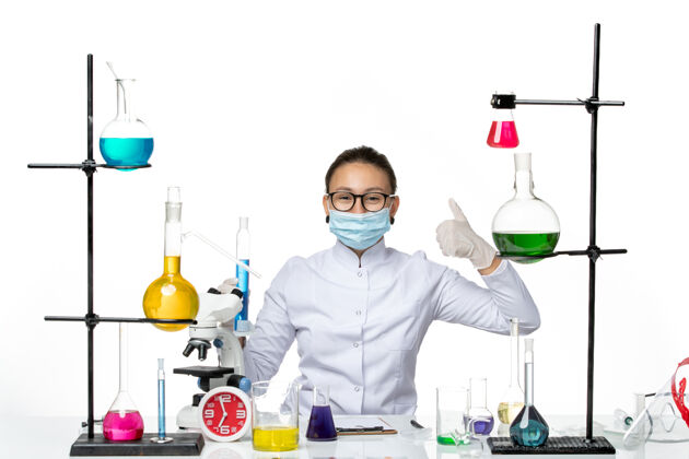 面具正面图：穿着医疗服的女化学家 戴着面具 拿着蓝色溶液的烧瓶 在白色背景上微笑 飞溅着病毒化学实验室的病毒喷溅医学医生