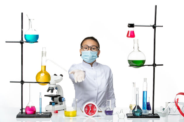 专业前视图：穿着医疗服的女化学家 戴着面罩 坐在白色背景上 化学实验室的病毒-病毒-飞溅医疗面罩解决方案
