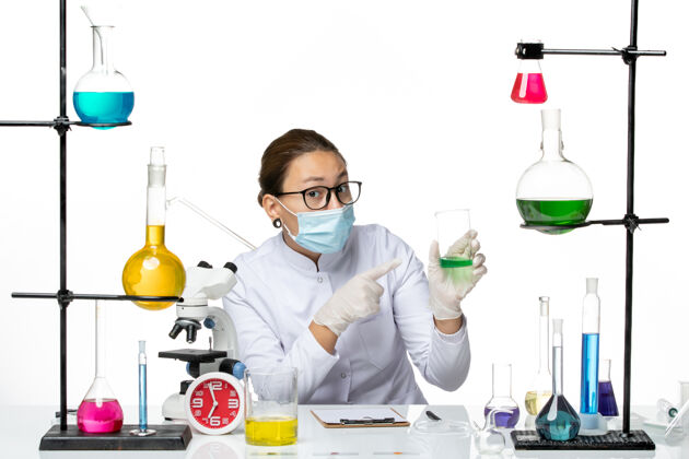 烧杯前视图穿着医疗服的女化学家 戴着面罩 白色背景上有绿色溶液 飞溅实验室病毒化学covid-前面化学喷溅