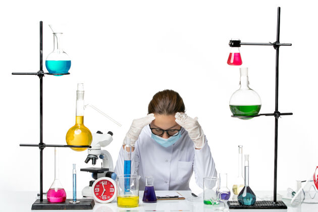 化学前视图穿着医疗服的女化学家戴着口罩坐在桌子前 白色背景上的解决方案疲惫不堪病毒化学实验室病毒飞溅医疗实验室桌子