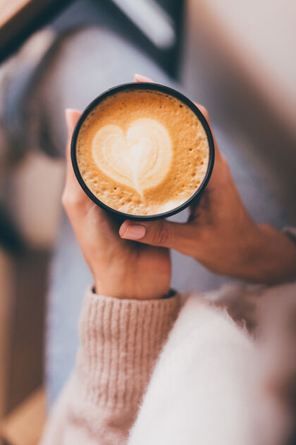 女人镜头中的女人手拿一杯热咖啡 用泡沫做成的心形图案举行艺术