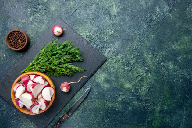 切割新鲜莳萝包和整个切碎萝卜刀的顶视图在黑色砧板的右侧 胡椒刀在绿-黑混合色背景上 有自由空间胡椒混合球