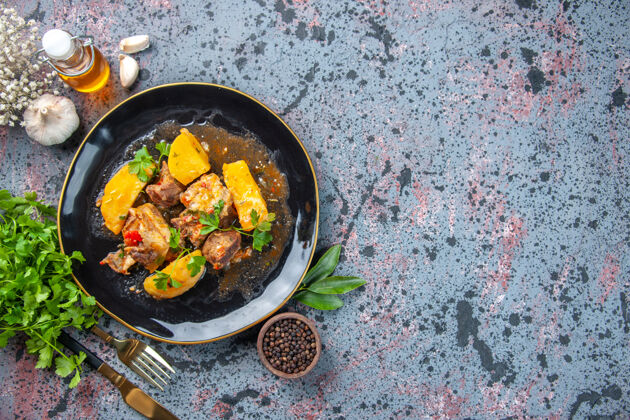胡椒美味的晚餐俯视图 黑色盘子里有绿色的土豆肉和胡椒蒜油瓶餐具大蒜瓶子饭