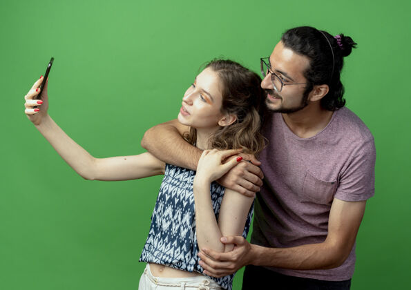 情侣一对年轻的男女 快乐的女人用智能手机在绿色背景上为他们拍照手机年轻拍摄