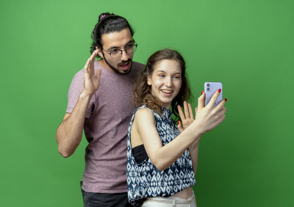 手机一对年轻的男女 快乐的女人用智能手机在绿色背景上为他们拍照照片年轻拍摄