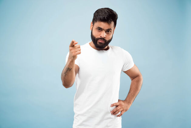 男人蓝色背景上穿着白衬衫的印度年轻人的半身特写肖像人类情感 面部表情 广告概念负面空间展示空酒吧 指向 选择 邀请帅哥工作成人