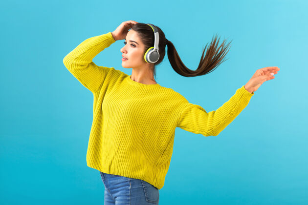耳机迷人时尚的年轻女子戴着无线耳机听音乐快乐地穿着黄色针织毛衣欢乐乐趣现代