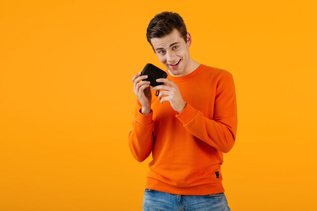 快乐时尚微笑的年轻人穿着橙色毛衣手持无线扬声器快乐地听音乐乐趣家伙模特
