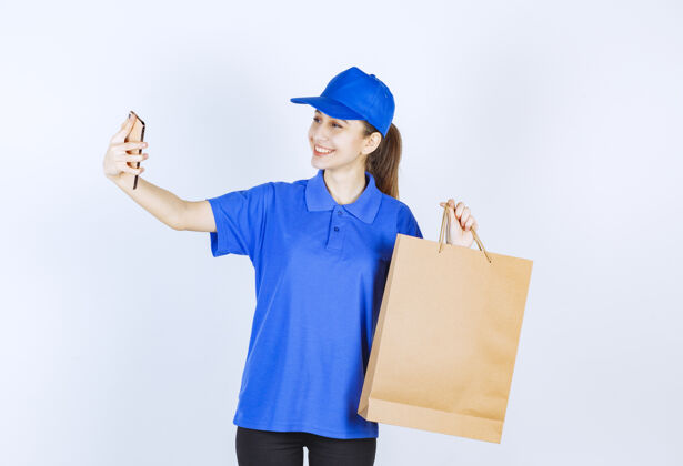 电话穿着蓝色制服的女孩拿着一个纸板购物袋 对着电话说话货物女员工