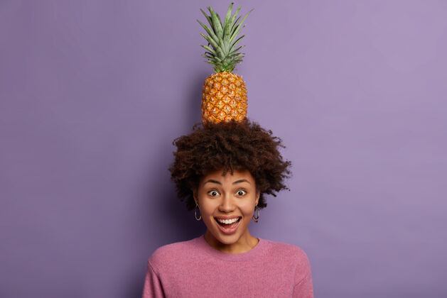 热带高兴的黑人妇女卷发 抱着菠萝头 咯咯地笑 享受夏天的休息 露出牙齿 盯着镜头请菠萝有机