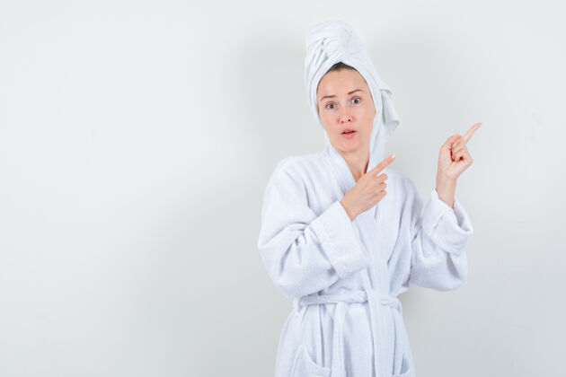 女孩画像中的年轻女子指着右上角的白色浴衣 毛巾和看困惑的前视图乐趣时尚浴袍