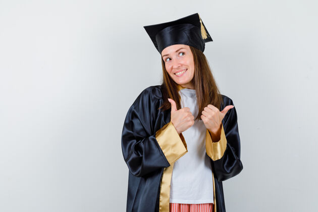 学术女毕业生的肖像 穿着制服 穿着休闲服 向上竖起大拇指 看上去很开心微笑大学毕业典礼
