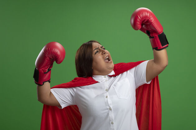 站立兴奋的中年女超级英雄戴着拳击手套站在格斗姿势孤立的绿色背景穿着中年战斗